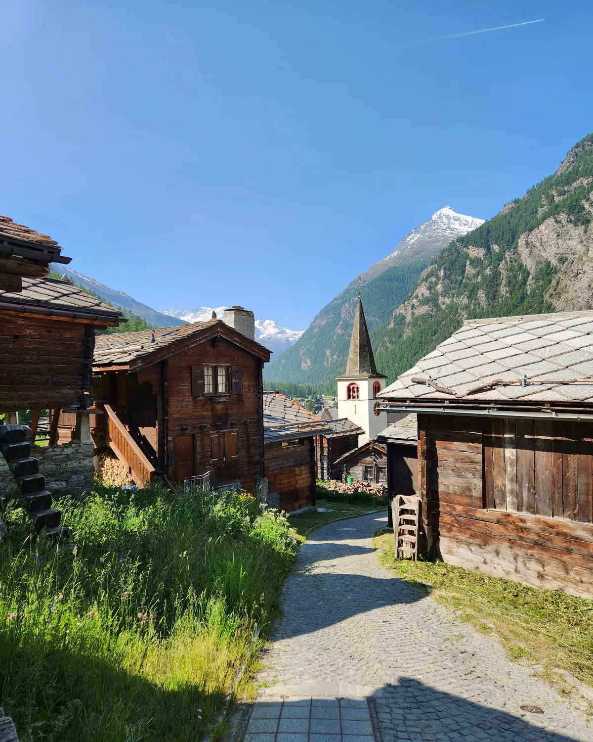 Traditional wooden alpine houses and church tower in Randa with mountains behind.
